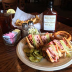 Famous Club Sandwich with sides of Onion Rings, Pickles, Fries, and Sauce.